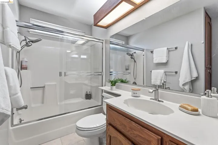 Bathroom featuring a shower/tub combination with sliding glass doors, a vanity with an integrated white sink, a chrome faucet, and a large wall-mounted mirror