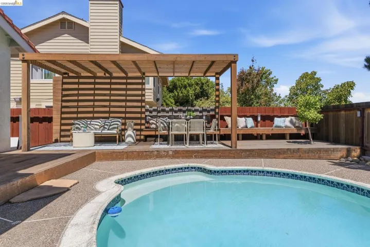 Resort-style backyard featuring a kidney-shaped swimming pool with tile trim, expansive concrete aggregate decking, and a multi-level wood deck