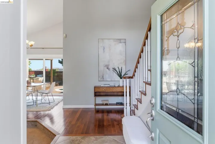 Entryway featuring a light blue front door with decorative glass, wood-finish flooring, a white staircase with wood handrails, and a vaulted ceiling in the background