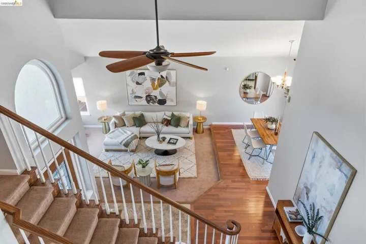 Vaulted ceiling living area with a ceiling fan, a large arched window, and wood-finish flooring