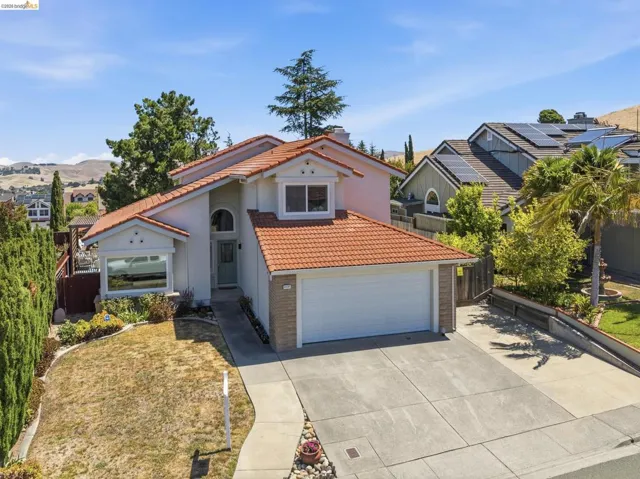 Two-story residence featuring a terracotta tile roof, an arched entry, a two-car garage, and a front yard with mature landscaping