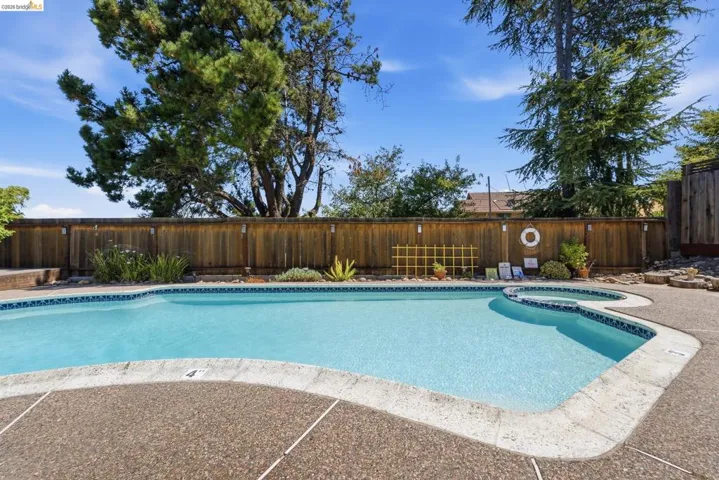 Backyard featuring a built-in swimming pool with an integrated spa, exposed aggregate decking, and perimeter privacy fencing