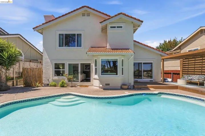 Rear exterior featuring a swimming pool with integrated steps, concrete hardscaping, stucco siding, a bay window, and a wooden pergola with slatted screening