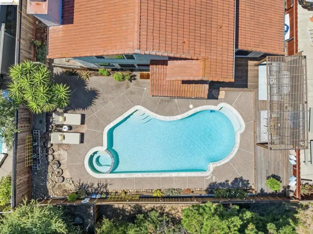 Curved in-ground swimming pool with integrated spa, surrounded by aggregate concrete decking and a wood deck with a slatted pergola