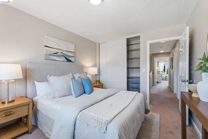 Light-toned walls complement plush carpeting in this bedroom featuring a built-in closet with shelving and drawer storage