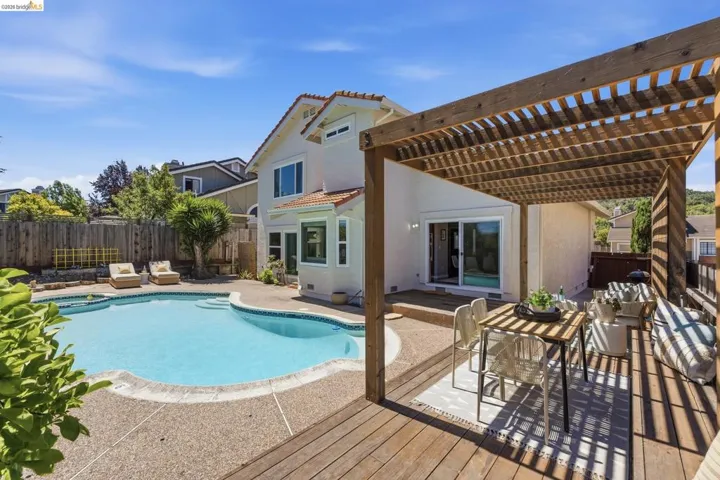 Outdoor living space featuring a spacious pool, expansive concrete decking, a wooden pergola-covered deck, a sliding glass door, and a private wooden fence