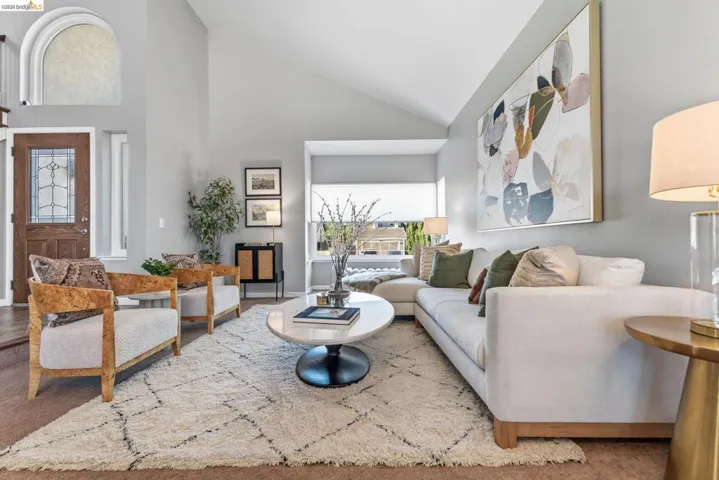Vaulted ceiling living space featuring an arched window, a leaded glass entry door, and an expansive window with a white roller shade