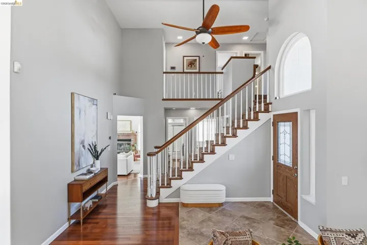 Entry foyer with soaring ceilings, wood-finish flooring, a grand staircase with white balusters and wood handrails, and an arched transom window