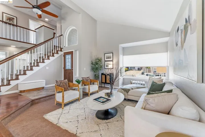 Open-concept living space featuring vaulted ceilings, wood-finish flooring, a two-story staircase with white balusters, and a decorative archway