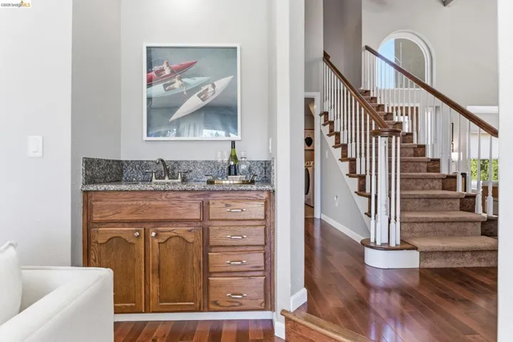 Hardwood flooring extending into the hallway, featuring a built-in wet bar with a granite countertop and wood cabinetry
