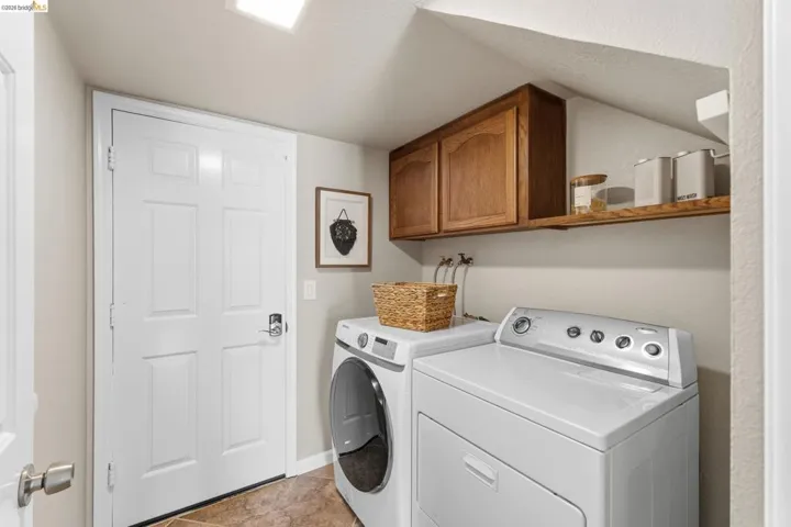 Dedicated laundry area featuring wood cabinetry, an open wood shelf, and neutral-toned wall paint