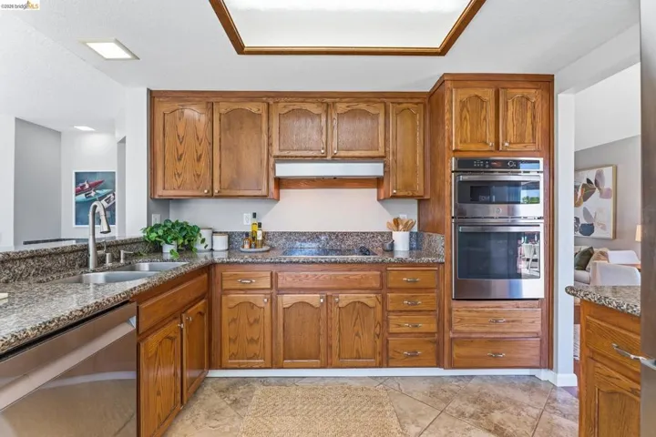 Kitchen featuring wood cabinetry, stainless steel appliances, granite countertops, and a double basin sink with a gooseneck faucet