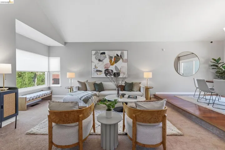 Living area featuring a stepped floor plan, corner windows with roller shades, and a distinct dining space with wood-finish flooring