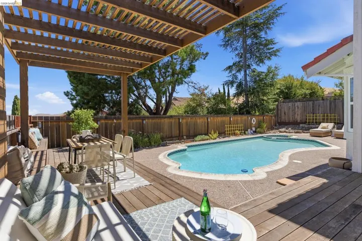 Outdoor living area featuring a custom-shaped swimming pool, a wood-finish deck, and a slatted wood pergola