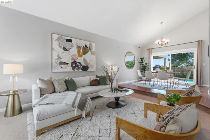 Vaulted ceilings enhance this open-concept living area with light gray walls and carpet flooring