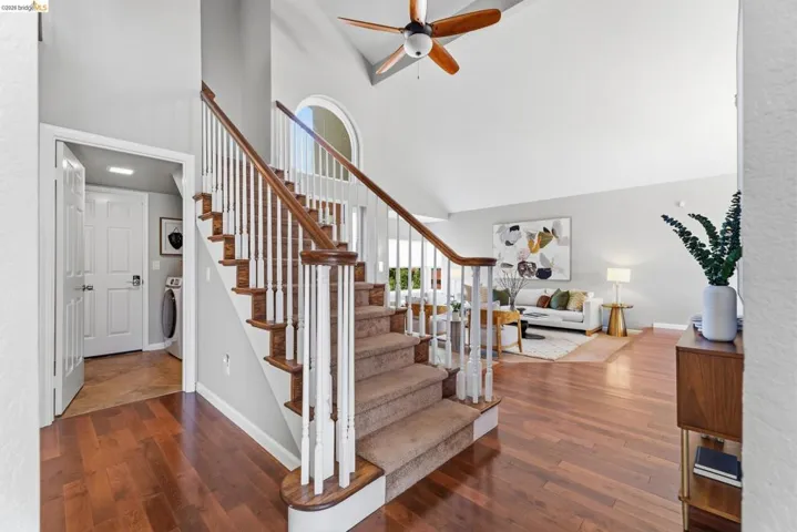 Two-story foyer with wood-finish flooring, carpeted staircase with white balusters, vaulted ceilings, and an arched window