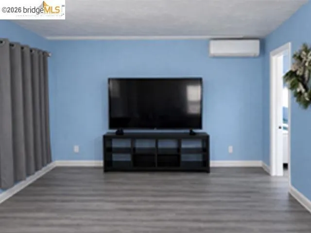 Spacious room featuring wood-finish flooring, light blue walls, and a wall-mounted mini-split system