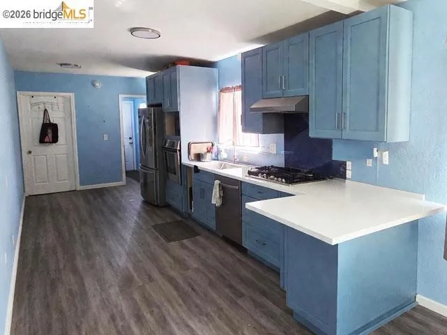 Kitchen featuring blue cabinetry, white countertops, stainless steel appliances, a gas cooktop, and wood-finish flooring