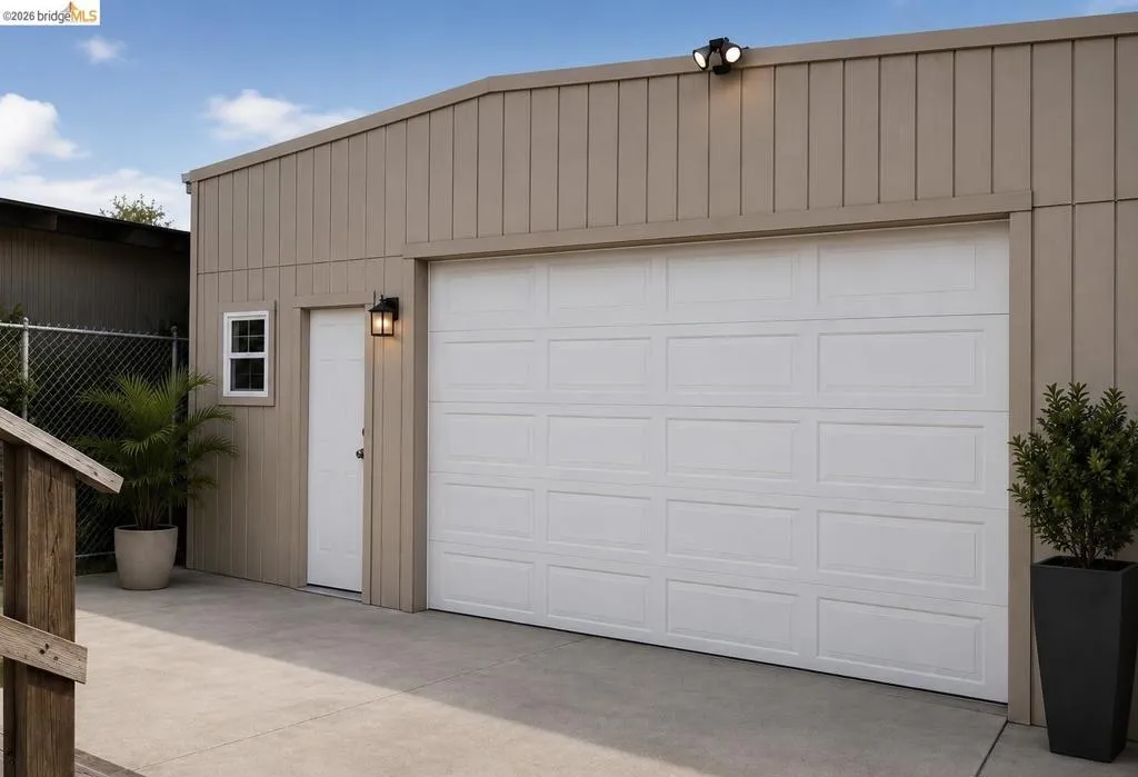 Single-panel garage door with recessed panels, adjacent pedestrian door, and exterior lighting fixtures