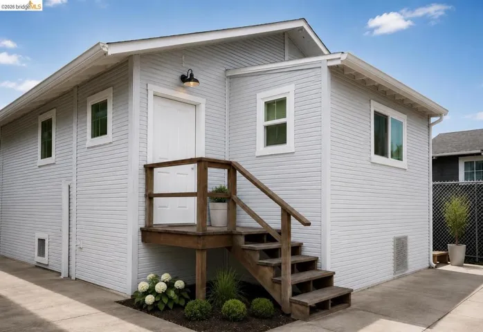 Exterior featuring light gray horizontal siding, white trim, and a prominent wood staircase leading to a white entry door