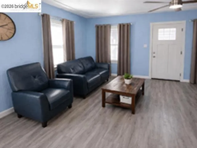 Living area featuring wood-finish flooring, two large windows, a ceiling fan with integrated lighting, and a paneled entry door with an upper window