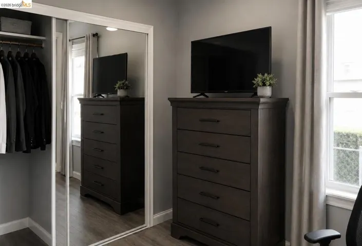 Spacious room featuring wood-finish flooring, a double-hung window with drapery, and a closet with mirrored sliding doors