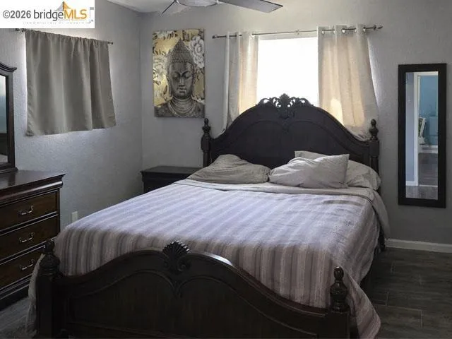 Bedroom featuring wood-finish flooring, two windows with drapery, and a ceiling fan