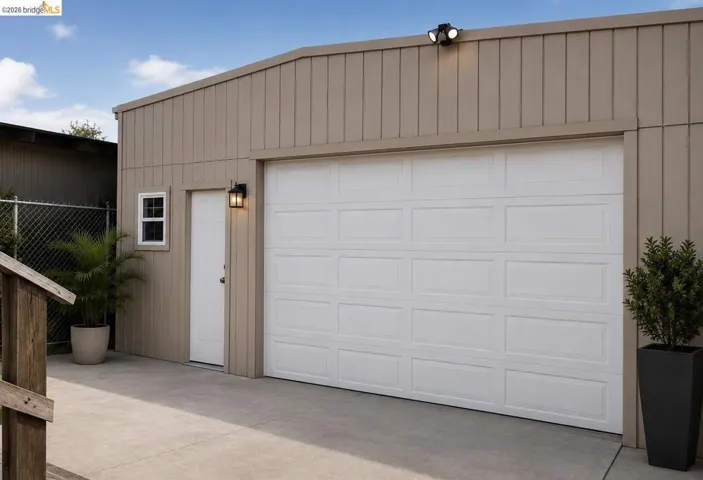 Single-panel garage door with recessed panels, adjacent pedestrian door, and exterior lighting fixtures