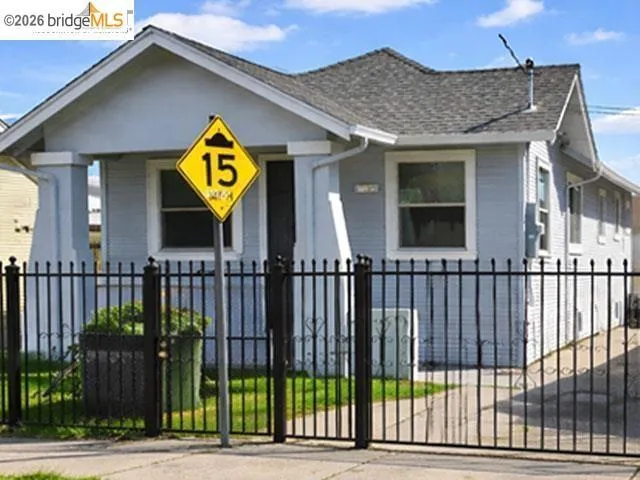 Light blue siding home with a gray shingle roof, featuring a black wrought iron fence and matching gate