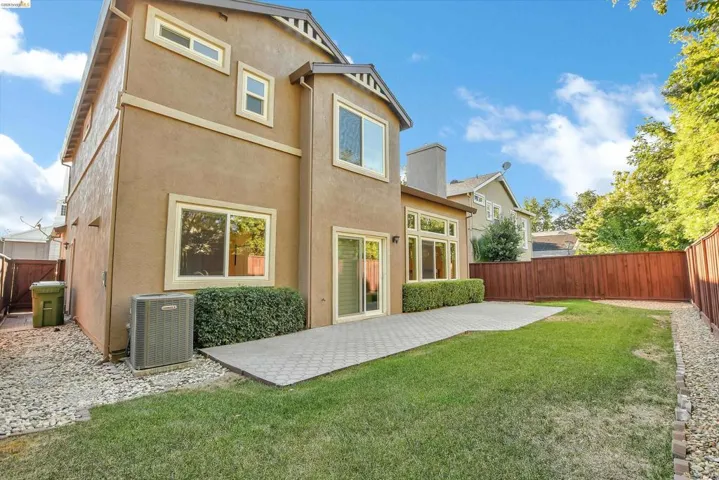 Rear exterior featuring a stucco finish, multiple windows, a sliding glass door, a paved patio, and a grassy yard with a wooden fence