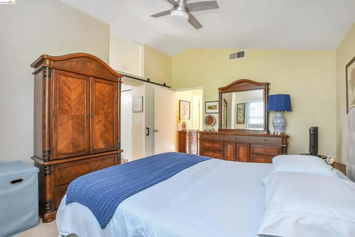 Vaulted ceiling with a ceiling fan, light-toned walls, and wood-finish flooring