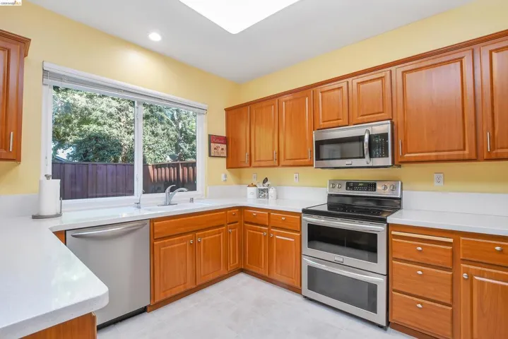 Kitchen with wood cabinetry, stainless steel appliances, light countertops, and a skylight