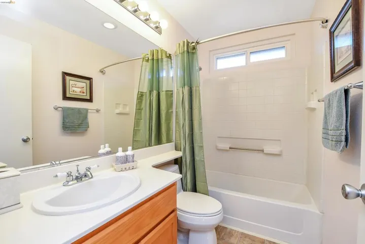 Full bathroom featuring a single vanity with an integrated sink, a large wall-mounted mirror, a tub/shower combination with white tile surround, and a clerestory window