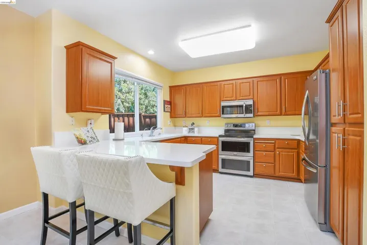 Kitchen featuring wood cabinetry, stainless steel appliances, a white countertop island, and light tile flooring