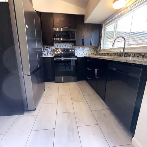 Kitchen featuring dark wood-finish cabinetry, stainless steel appliances, mosaic tile backsplash, and light tile flooring