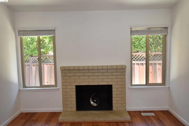 Brick fireplace with a tiled hearth, framed by two windows featuring privacy blinds and wood-finish flooring
