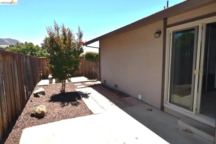 Private backyard patio with a stucco exterior, featuring a wood fence, concrete hardscaping, and a sliding glass door