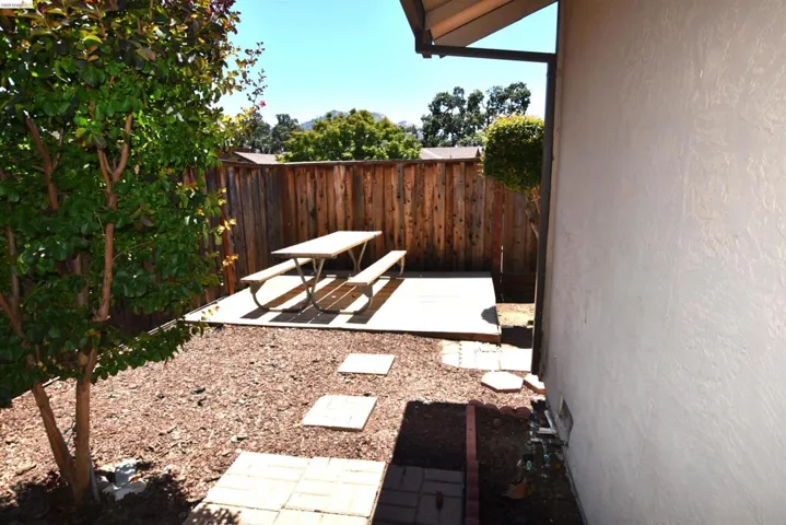 Private outdoor patio area featuring a wooden privacy fence, a concrete patio slab, square paver stepping stones, and a mulched ground cover