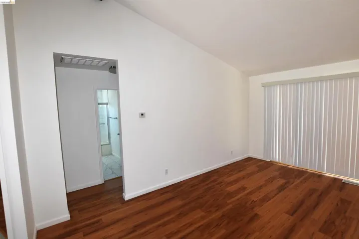 Spacious room featuring wood-finish flooring, white baseboards, and a vaulted ceiling
