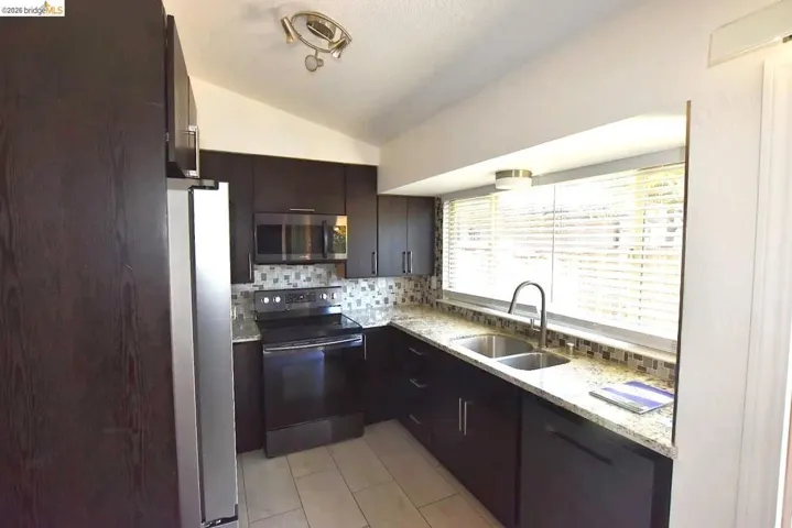 Contemporary kitchen with dark wood-finish cabinetry, granite-style countertops, stainless steel appliances, and mosaic tile backsplash