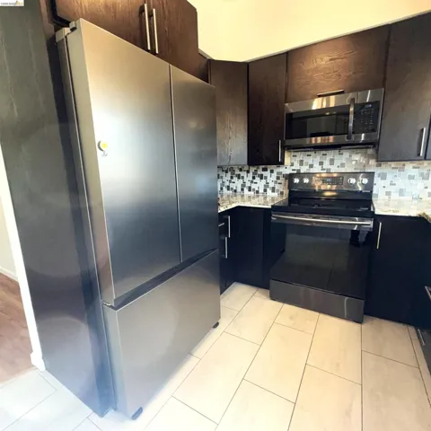 Full kitchen featuring stainless steel appliances, dark wood-finish cabinetry, light-toned tiled flooring, and a mosaic tile backsplash