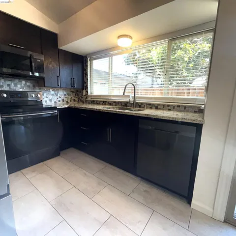 Modern kitchen featuring dark cabinetry, a mosaic tile backsplash, and light-toned plank flooring