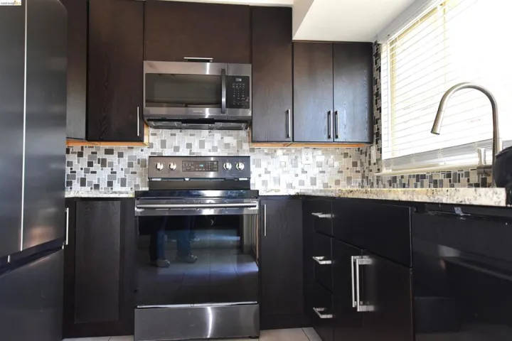 Modern kitchen featuring dark wood-finish cabinetry with silver hardware, a stainless steel over-the-range microwave, and a black electric range