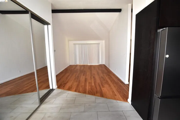 Spacious interior featuring vaulted ceilings, wood-finish flooring, white walls, and a sliding glass door with vertical blinds