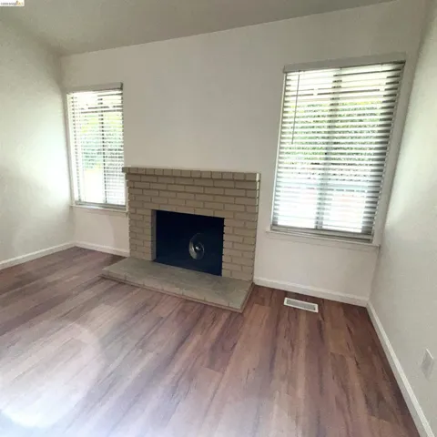 Living space featuring wood-finish flooring, a brick fireplace with a stone hearth, and two windows with blinds