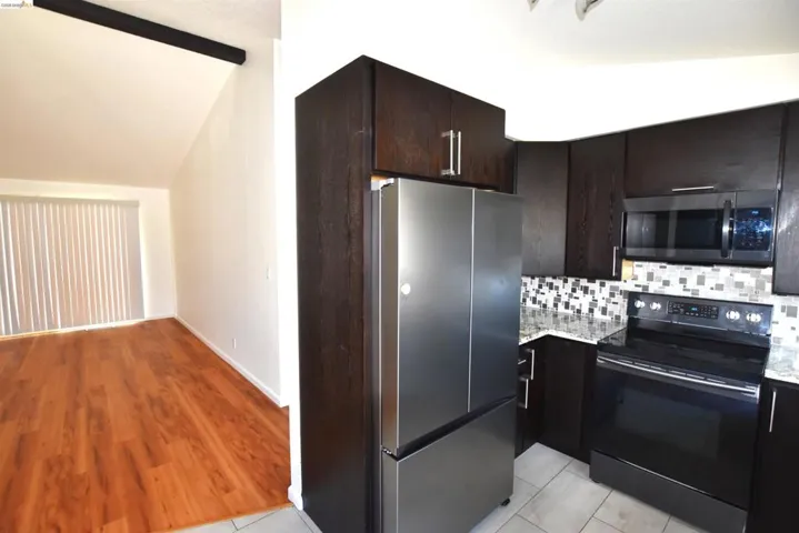 Kitchen featuring dark wood-finish cabinetry, stainless steel appliances, speckled countertops, and a mosaic tile backsplash