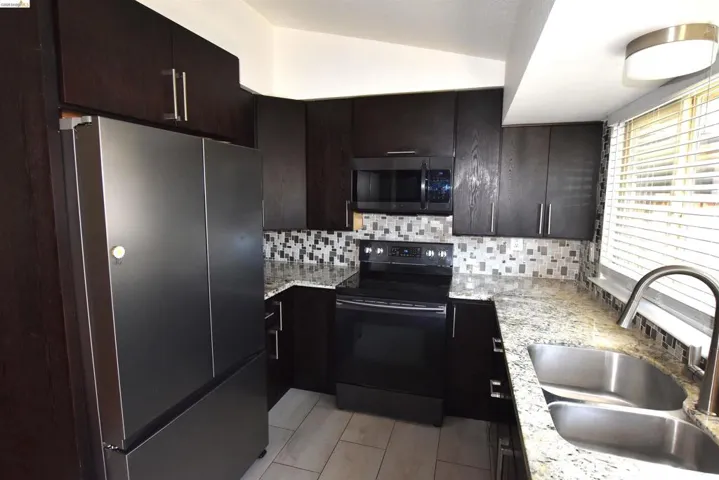 Well-appointed kitchen featuring dark wood-finish cabinetry with brushed nickel hardware, light-toned stone countertops, and a full tile backsplash