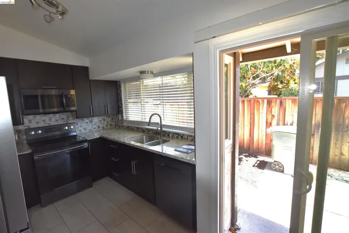 Modern kitchen featuring dark wood-finish cabinetry, light speckled countertops, a mosaic tile backsplash, and stainless steel appliances