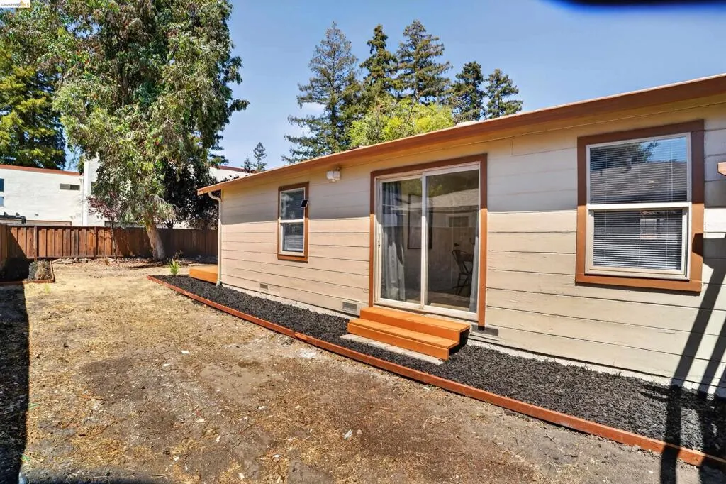 Rear exterior featuring beige horizontal siding, a sliding glass patio door, and two windows with brown trim