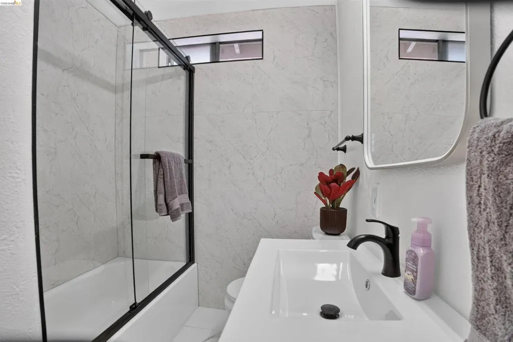Bathroom featuring a white vanity with an integrated sink, matte black faucet, and a contemporary frameless mirror